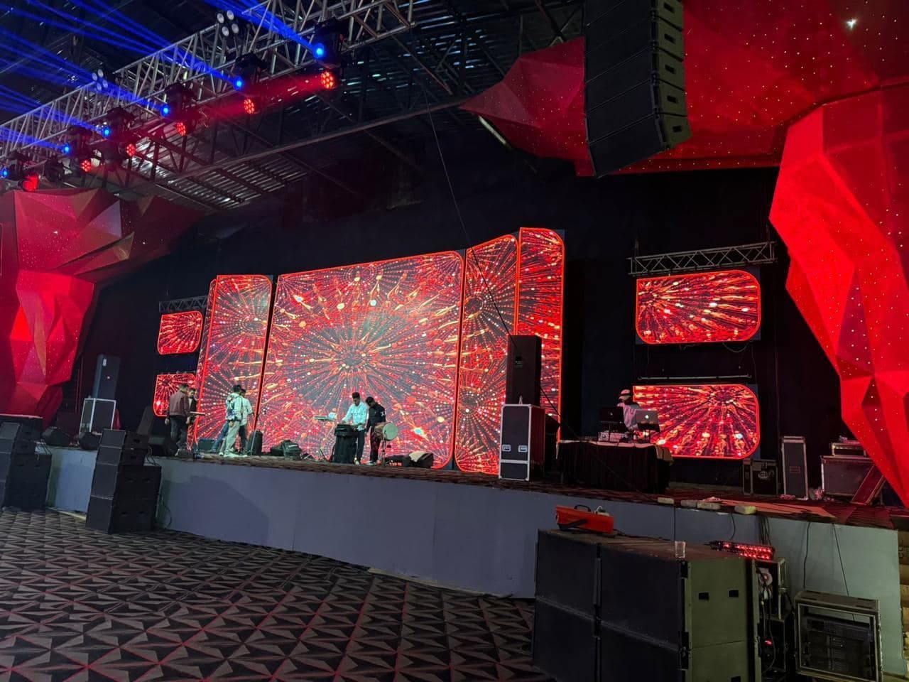 A large indoor LED video wall and side panels lit red above a truss-framed stage in a Siliguri hall