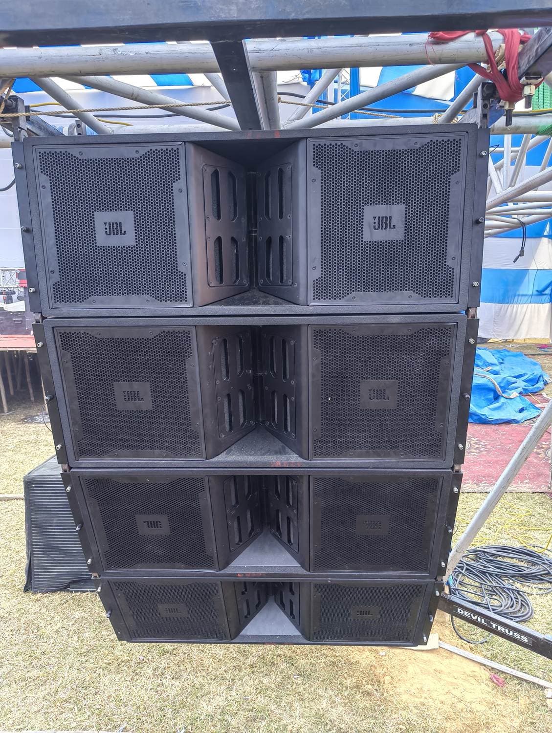 JBL line-array cabinets ground-stacked three high under truss on an open ground