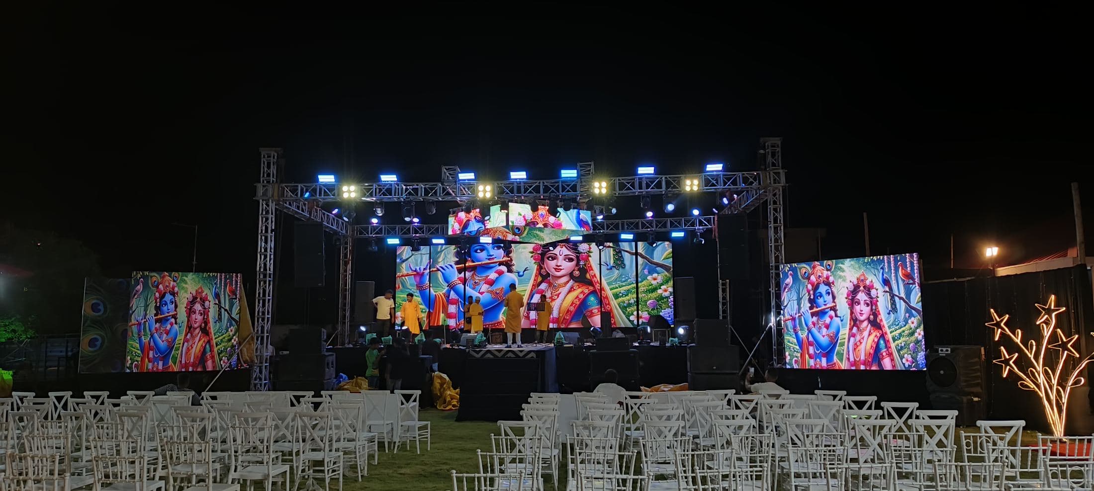 Outdoor night stage in North Bengal with a centre LED screen, two side LED panels and rows of guest chairs